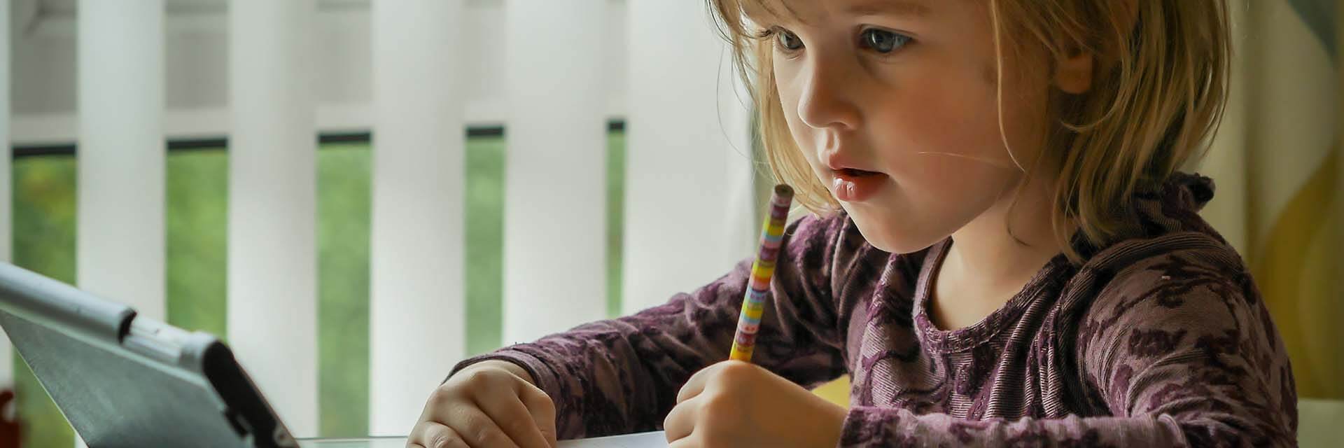 Konzentration bitte Kind sitzt am Tisch und blickt konzentriert auf ein Ipad, mit Stift in der hand