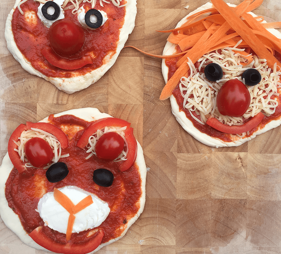 Pizza mit Toppings, angerichtet wie gesichter. Dazu die FruchtBar Tomatensoße